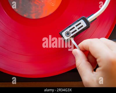 Detail einer männlichen Hand, die die Nadel auf die Spur einer roten Vinylplatte legt. Klassischer Plattenspieler Stockfoto