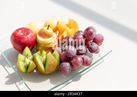 Rohe Früchte Beeren Platter, Mango, Orangen, Kiwi, Erdbeeren, Blaubeeren grapefruit Trauben, Bananen, Äpfel auf dem weißen Teller, auf dem Weg von weißen Tabl Stockfoto