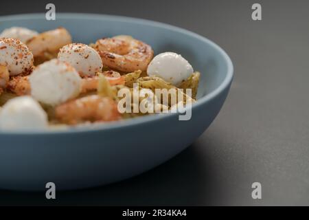 Penne-Pasta mit Garnelen und Mozzarella und Pesto in blauer Schale mit Kopierfläche, flacher Fokus Stockfoto