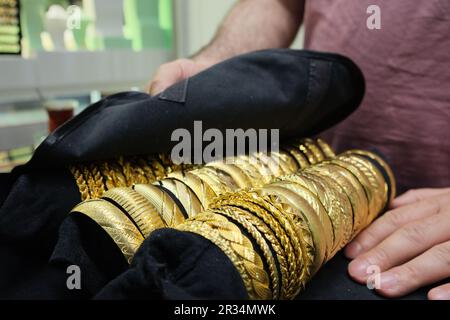 Luxuriöse goldene Armbänder, drei Reihen imitierter goldener Armbänder auf schwarzem Schmuckhintergrund. Stockfoto