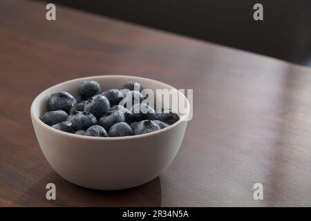 Frisch gewaschene Heidelbeeren in weißer Schüssel auf Walnusstisch, flacher Fokus Stockfoto