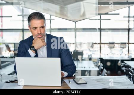 Seriöser, reifer Geschäftsmann, der mit einem Laptop am Schreibtisch sitzt. Stockfoto