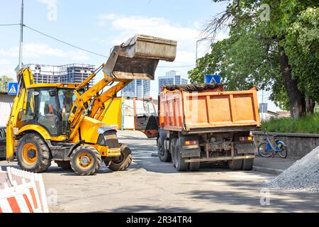 Straßenbaumaschinen, ein Traktor mit hydraulischem Löffel und ein alter Lkw an einem sonnigen Tag an einer Gabelung in einer Stadtstraße. Stockfoto