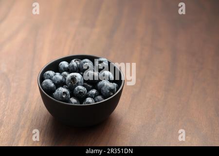 Große Bio-Heidelbeeren in einer schwarzen Schüssel auf Walnusstisch, flacher Fokus Stockfoto