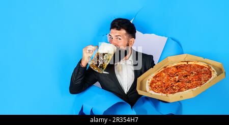 Bärtiger Mann mit leckerer Pizza, der Bier trinkt. Pizza-Zeit. Zufriedener Mann mit leckerer Pizza und kaltem Bier, der durch das Papierloch schaute. Fastfood Stockfoto