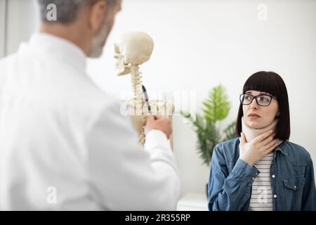 Schulterblick einer schönen jungen Frau mit Halsspange und Blick auf das menschliche Skelett eines erwachsenen Mannes. Beunruhigte Frau in Brille, die nach einer Wirbelsäulenverletzung einen Arzt zur Beratung besucht. Stockfoto