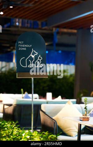 Ein haustierfreundliches Café-Schild auf einer sonnigen Sommerterrasse lädt Haustierbesitzer ein, sich zu entspannen und eine Mahlzeit mit ihren pelzigen Freunden zu genießen. Die warme, einladende Atmosphäre Stockfoto