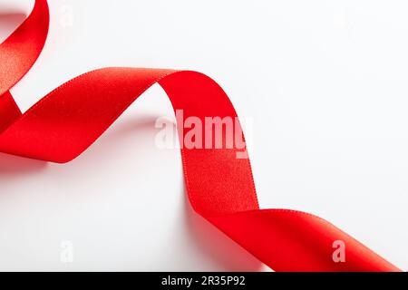 Rotes Seidenband zum Einwickeln von Geschenken auf weißem Hintergrund. Locken aus dekorativem Weihnachtsband. Element für Konstruktion. Stockfoto