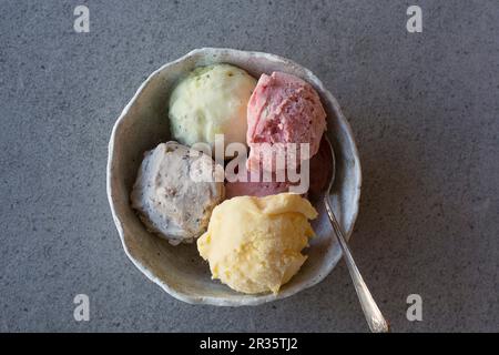 Hausgemachtes Eis (Mango, Erdbeere, Heidelbeere und Limette) in einer Schüssel mit einem Löffel Stockfoto