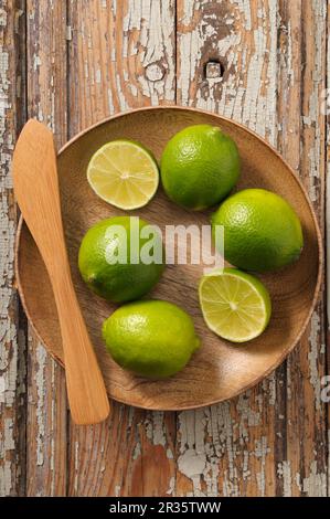 Limetten, ganz und halbiert, in einer Holzschüssel Stockfoto