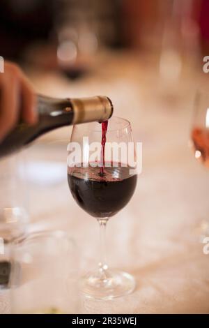 Rotwein wird aus einer Flasche in ein Glas gegossen Stockfoto
