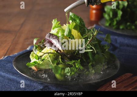 Olivenöl wird über Eisbergsalat gegossen Stockfoto