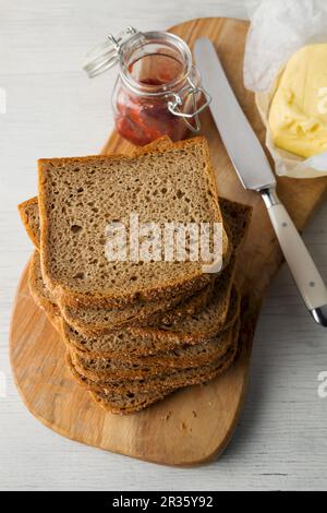 Scheiben Vollkornbrot auf einem Holzbrett mit Butter und Erdbeermarmelade gestapelt Stockfoto