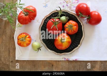 Ein Arrangement aus hausgewachsenen Weintomaten auf einer bestickten Tischdecke Stockfoto