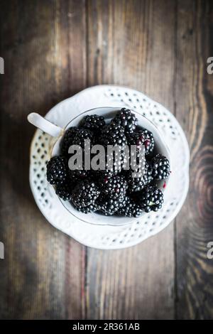 Frische Brombeeren in einer Teetasse auf einem Holztisch Stockfoto