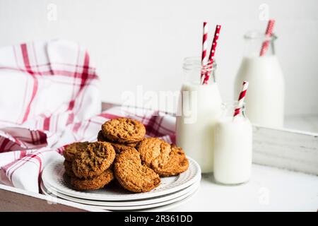 Haferbrei-Kekse und Milchflaschen auf einem weißen Holztablett Stockfoto