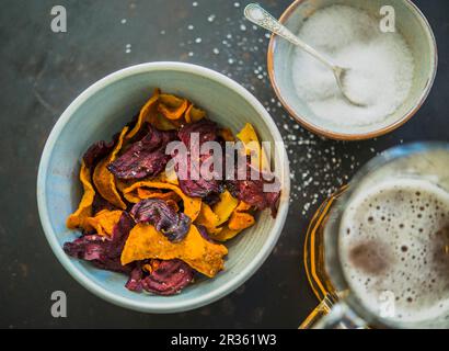 Bunte Gemüse-Chips (Karotten, Pastinaken und Rote Bete) mit Salz und einem Bier Stockfoto