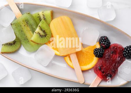 Teller mit köstlichem Eis am Stiel, Eiswürfeln und frischem Obst auf weißem Hintergrund, Draufsicht Stockfoto