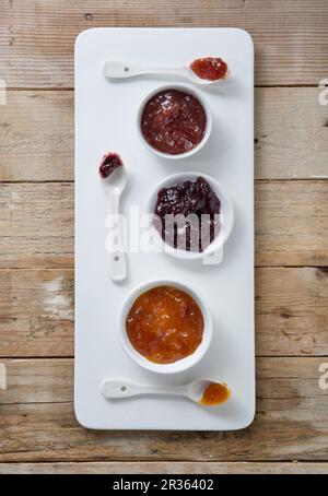 Drei Arten von Marmelade in Schüsseln mit Löffeln auf einem Brett Stockfoto
