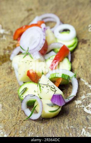 Zwiebelringe, in Scheiben geschnittene Kartoffeln, Zucchini und Paprika Schichten auf einer hölzernen Schneidebrett Stockfoto