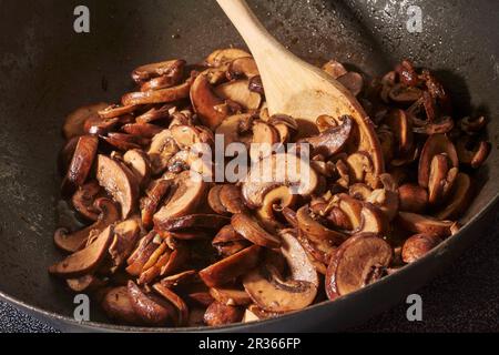 Braune Pilze werden mit gehacktem Knoblauch in Olivenöl in einem Wok gebraten Stockfoto