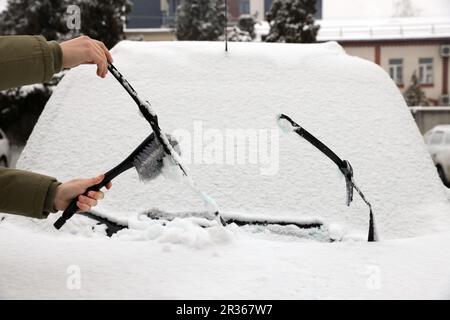 Frau, die Wischerblätter von Schnee säubert, mit Bürste im Freien, Nahaufnahme Stockfoto