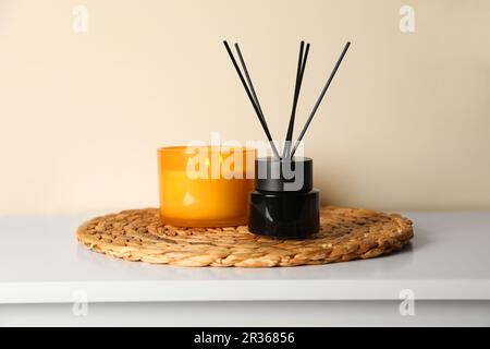 Aromatischer Schilf-Lufterfrischer und Kerze auf weißem Tisch im Innenbereich Stockfoto