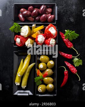 Verschiedene Oliven, gefüllte Mini-Paprika und jalapeños auf einem schwarzen Backblech Stockfoto