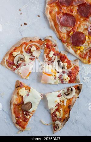 Eine Pizza mit Tomaten, Pilzen, Zwiebeln, gewürfeltem Speck, Spiegelei (in Scheiben geschnitten) und eine Salami-Pizza Stockfoto