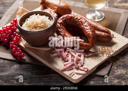 Würstchen, Sauerkraut und Speckstreifen auf einem Holzbrett Stockfoto