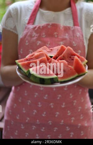 Eine Frau das Tragen einer Schürze, die eine Platte von Melone Schichten Stockfoto