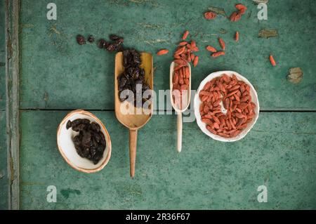 Getrocknete Preiselbeeren und Goji-Beeren in Holzschaufeln und Schalen auf einer rustikalen Holzoberfläche Stockfoto