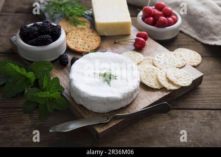 Eine Käseplatte mit Sesamsamen und Weizencrackern, Kräutern, Kirschen und Brombeeren Stockfoto