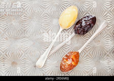 Zitronenkurz, schwarze Kirschmarmelade und Orangenmarmelade auf Vintage-Löffeln Stockfoto