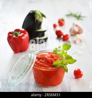 Ein Glas mit Ajvar und frische Zutaten im Hintergrund Stockfoto