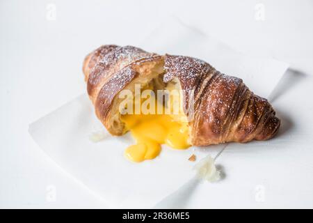 Ein Croissant gefüllt mit gesalzenem Eigelb, aufgeschnitten auf Backpapier Stockfoto