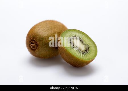 Eine ganze Kiwi und eine halbierte Kiwi auf einer weißen Oberfläche Stockfoto