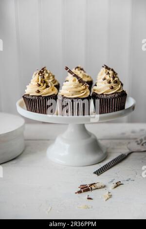 Schokoladen-Cupcakes mit weißer Schokoladenglasur auf einem Kuchenstand Stockfoto