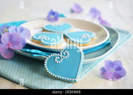 Herzförmige Kekse mit blau-weißen Glasur, serviert auf einem Teller mit Blumen Stockfoto