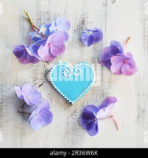 Herzförmige Kekse mit blauem und weißem Glasur, umgeben von Blumen Stockfoto