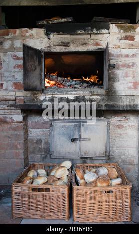 Ein glühender Holzofen und frisch gebackene Brötchen in Korbkörben Stockfoto