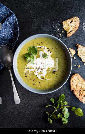 Eine Schüssel Erbsen- und Brunnenkresssuppe mit Sauerrahm und Brot Stockfoto