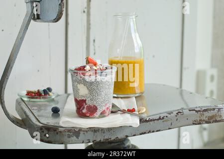 Ein Chia-Pudding mit Sommerfrüchten und Nüssen in einem Glas und ein Mango-Orangen-Smoothie mit Chiasamen auf einem alten Stuhl Stockfoto