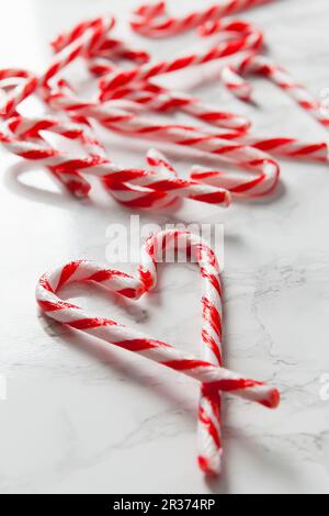 Weiße Marmoroberfläche mit Zuckerstangen und zwei Zuckerstangen im Vordergrund, die eine Herzform bilden Stockfoto