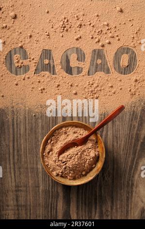 Kakaopulver in einer Schüssel und verschüttet auf einem Holzhintergrund mit dem Wort „Kakao“ Stockfoto