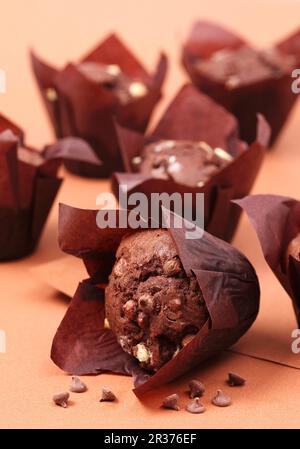 Mehrere doppelte Schokoladen-Muffis in schokoladenfarbenen Cupcake-Kästen auf einem schokoladenfarbenen Hintergrund Stockfoto