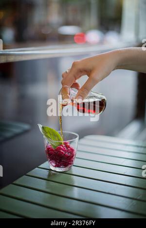 Eine Hand gießen Kräuterlikör auf Granatapfel Granita in einem Glas Stockfoto