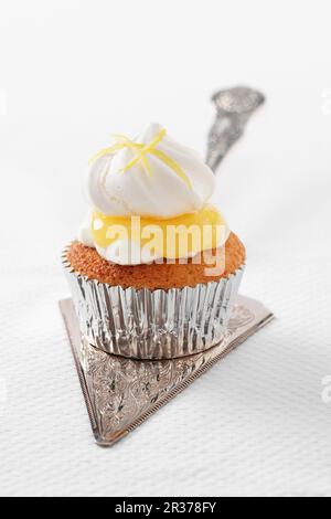 Ein einzelnes Zitronen-Baiser-Cupcake mit ZitronenQuark in einem silbernen Etui auf einem silbernen Kuchenstück Stockfoto