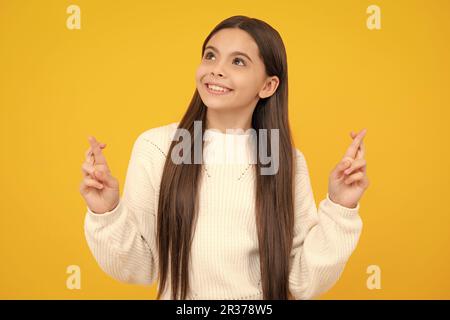 Froh Teenager-Mädchen kreuzt die Finger, erwarten, gute Nachrichten zu hören, isoliert gelben Hintergrund. Glückliches Kind freut sich, dass seine Träume wahr wurden. Exziteme Stockfoto