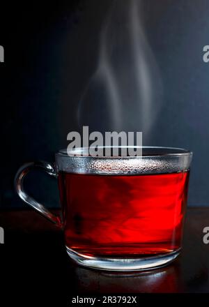 Hot red berry Obst Kaffee in einem Glas Becher mit Dampf stehend auf einem dunklen Holz mit dunkelgrauer Hintergrund Stockfoto